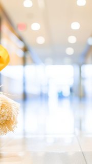 Cleaning cart loaded with a mop and broom stands in the hallway of an office building as background.