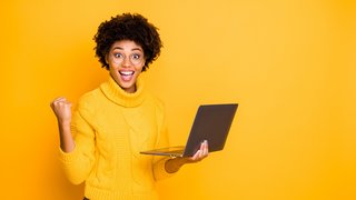 Portrait of her she nice attractive lovely charming smart clever cheerful wavy-haired girl holding in hands laptop celebrating winning isolated over bright vivid shine vibrant yellow color background