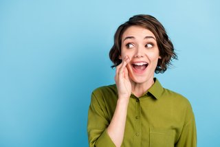 Photo portrait of young pretty girl with short hair telling secret information rumouring gossiping wearing green shirt isolated on blue color background